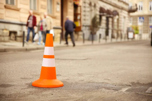 Reparação sinal de trabalho restringindo o tráfego. Branco-laranja plástico listrado cone aviso de perigo. A apertar no trânsito. Rua da cidade velha com carros. Reparação de estradas. Pobre asfalto na estrada — Fotografia de Stock