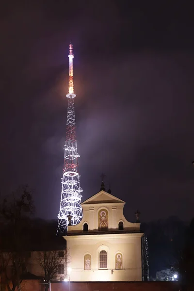 Львов, Украина - 1 9 2020: пейзаж ночного города. Католическая церковь и телебашня. Радиопередача на расстоянии. Телекоммуникационные технологии. Огни древнего туристического города — стоковое фото