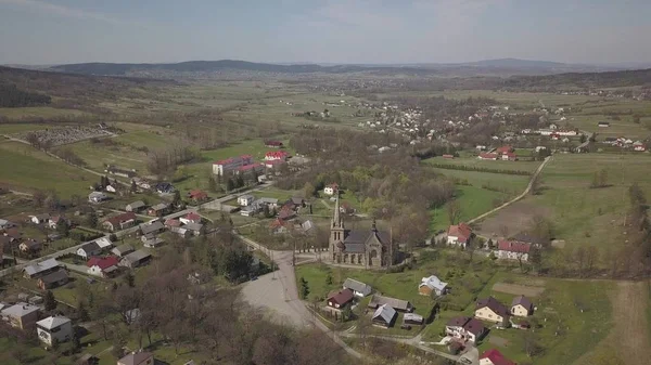 Cieklin, Polen - 4 9 2019: Panorama van een klein Europees dorp met een katholieke kerk in het centrum. Boerderijen tussen groene pittoreske heuvels. Panorama van de Karpaten met een drone — Stockfoto