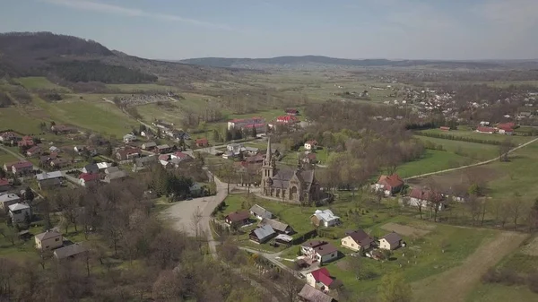 Cieklin, Polsko - 4 9 2019: Panorama malé evropské vesnice s křesťansko-katolickým kostelem v centru. Farmy mezi zelenými malebnými kopci. Panorama Karpatské oblasti s dronem — Stock fotografie