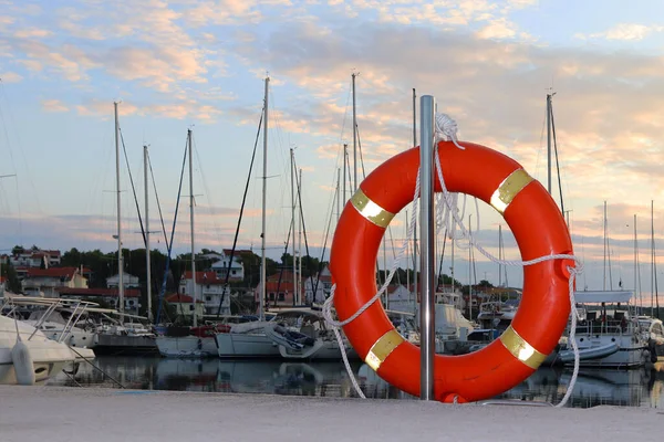 Помаранчевий довічне кільце на пристані в хорватських Марина на тлі парусних яхт. Безпека на води і збереження, утоплення. Устаткування портового міста. Спорядження рятувальні команди — стокове фото