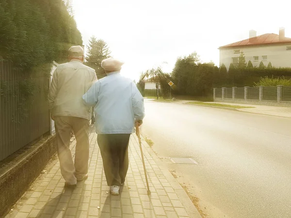 Une paire de personnes âgées marchent le long du trottoir le long de la route en se tenant la main. Grand-père et grand-mère en promenade dans un quartier résidentiel. Mouvement santé des personnes âgées. Bonne vieillesse — Photo