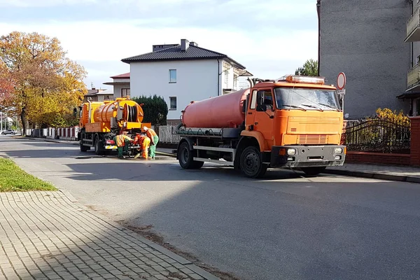 Riolering wissen met speciale technische middelen op de straten van een kleine Europese stad. Oranje auto's en gemeentelijke werknemers schoon de stad van puin en vuil. Infrastructuur — Stockfoto
