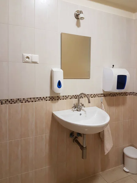 Interior del baño en colores beige claro y blanco. Lavabos redondos de cerámica. Espejos, jabonera de plástico y grifos cromados para lavarse las manos después de un inodoro. Diseño con azulejos de revestimiento oscuro —  Fotos de Stock