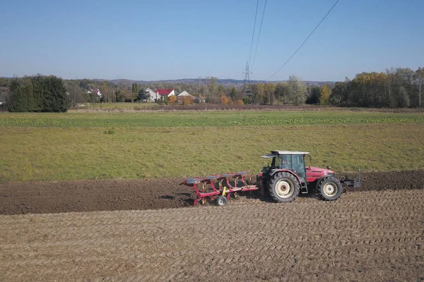 Un agriculteur sur un tracteur rouge avec un semeur sème du grain dans des terres labourées dans un champ privé dans la région du village. Mécanisation des travaux sur le terrain. La vie quotidienne du fermier. Traitement des terres. L'agraire — Photo