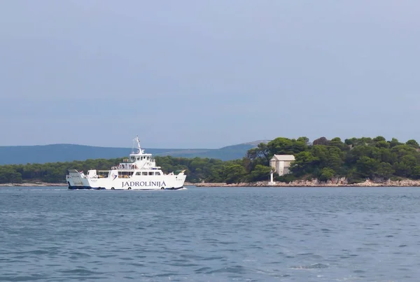 Dalmatien, Kroatien - 9 9 2018: Europa. Medelhavsområdet. Adriatiska havet. En färja-Katamaran segling förbi en ö av lummiga gröna pinjeträd och en signalering fyr. Trans. av passagerare — Stockfoto