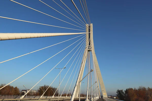 Rzeszow, Lengyelország - 9 9 9 2018: Felfüggesztett közúti híd át a Wislok folyón. Fémkonstrukciós technológiai szerkezet. Modern építészet. A kék hátterű fehér kereszt a város szimbóluma. — Stock Fotó
