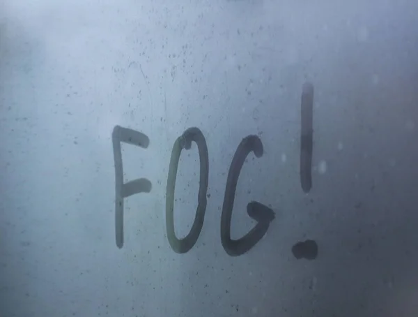 Надпись - туман, написанный пальцем на туманном стекле с капельками мкрими. Предупреждаю автомобилистов об опасности на дорогах. Безопасность движения. Прогноз погоды. Белая саван за окном — стоковое фото