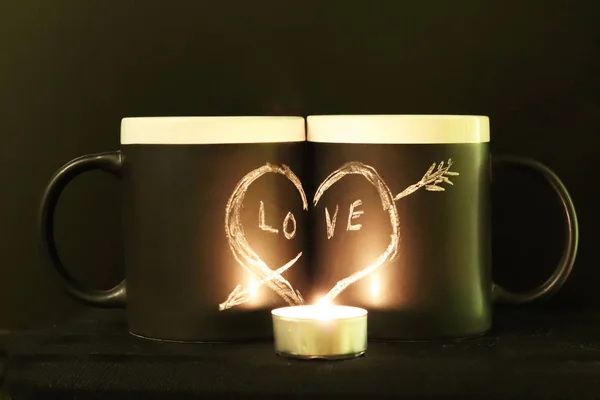 Two black circles with a symbol of love with a red candle and a branch of spruce. Heart pierced by an arrow drawn in white chalk on a black background. Valentine's Day. The romance of the relationship