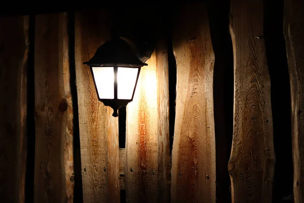 Noite a lanterna brilha em uma velha cerca de madeira com portão e pilar de concreto — Fotografia de Stock