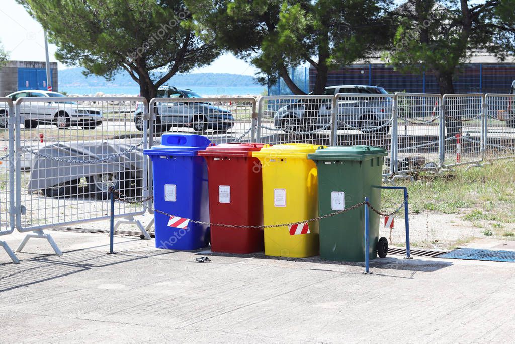 Four multicolored boxes for sorted garbage: red, green, blue and yellow. Recycling garbage in the tourist area. Infrastructure of the Mediterranean marina. Plastic waste containers