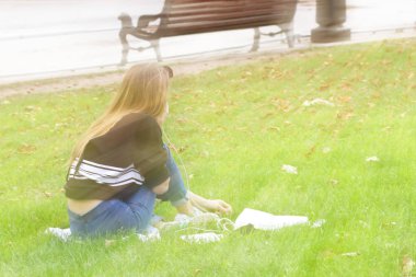 Genç bir kız bir çim bir cep telefonu üzerinde konuşurken bir antik kent Park'ta oturuyor. Sonbahar çimleri düşen yapraklar ile. İletişim ve eğlence modern gençlik. Avrupa şehri Lviv Ukrayna