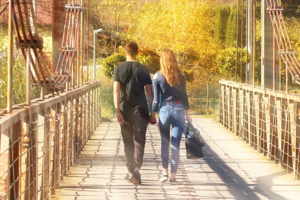 Pareja joven: el chico y la chica caminan sobre el puente en el otoño tomados de la mano. Relaciones románticas entre un hombre y una mujer. La manifestación de amor entre las personas. Camina al aire libre. Manera común —  Fotos de Stock