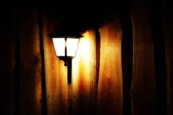 Lâmpada de rua brilhante no fundo de uma cerca de madeira à noite. A luz permeia a escuridão. Iluminação pública. Criando uma atmosfera acolhedora e romântica. Elementos de cenário e design — Fotografia de Stock