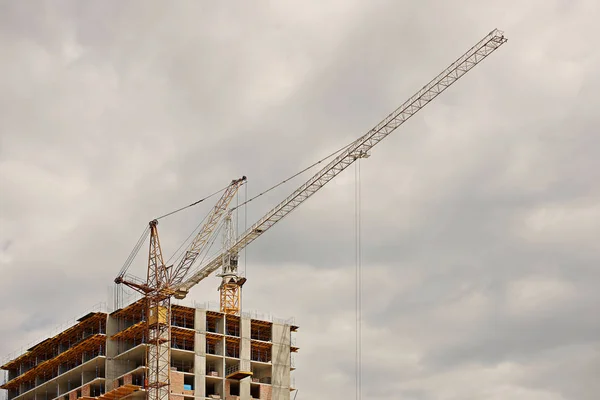 Gruas-torre trabalham durante a construção de um edifício de vários andares. Novos apartamentos para residentes e instalações para escritórios. Trabalho arriscado em altura. Levantamento de materiais de construção pesados. Desenvolvimento da cidade — Fotografia de Stock