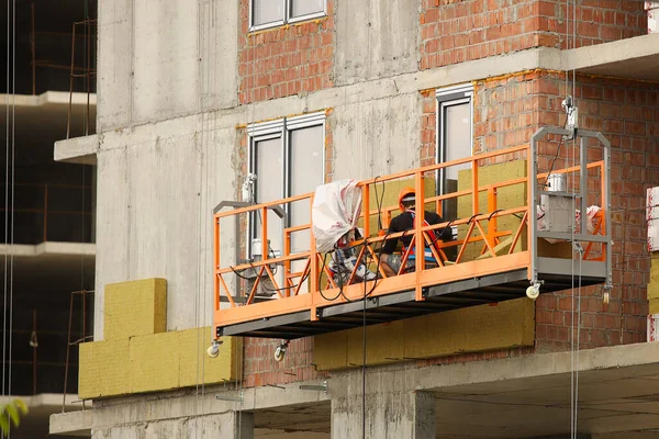 Due operai in un cesto isolano la parete vetrata di un edificio a più piani. Misure di sicurezza in cantiere durante i lavori in quota. Isolamento termico degli spazi abitativi per risparmiare — Foto Stock