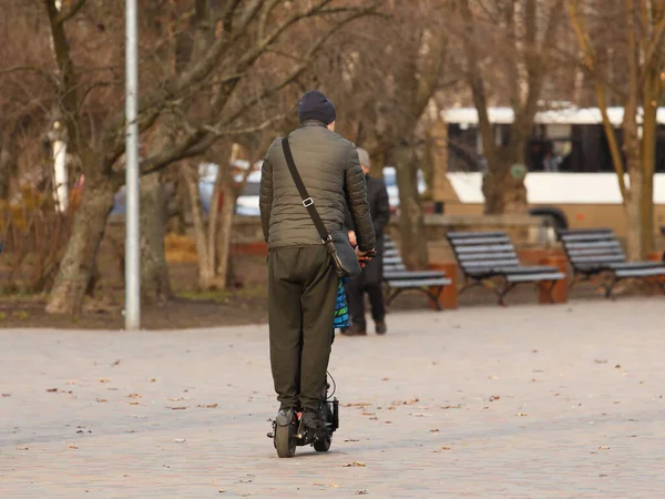 Un hombre monta un scooter eléctrico en el parque en un soleado día de primavera. Actividad para el desarrollo armonioso de la población. Llegar a casa del trabajo a la hora pico. Equilibrio en un transporte de dos ruedas — Foto de Stock