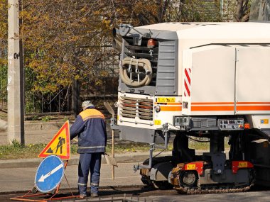 İşçi yol işareti koyuyor. Ağır makineler kullanarak asfalt kaldırma. Yol yapımı ve onarımı. Katı yüzeyi olan bir otoyol inşa etmenin modern teknolojisi. İnsanlar inşaat alanında çalışıyor.