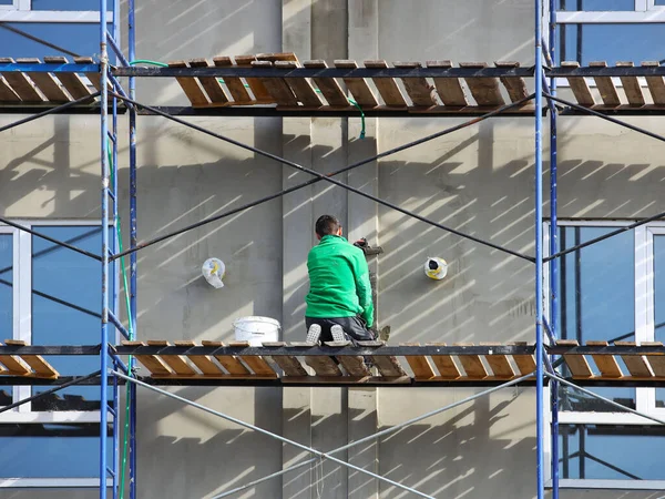 一个站在脚手架上的工人在建筑立面贴上石板 建造一座高楼的建筑工程 高层建筑工程的安全措施 薄片的绝缘性 — 图库照片