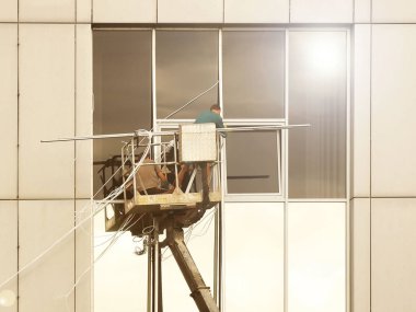Bir kaldırma platformundaki iki işçi yüksek bir binanın dışındaki bir pencereyi tamir ediyorlar. Gökdelenlerin camlarını siliyorum. Yüksek irtifa çalışması tehlikesi. Gökdelenlerin onarımı ve bakımı.