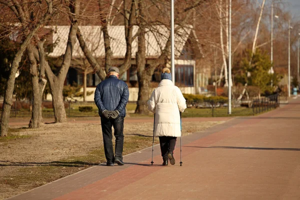 Elderly couple on a walk with sticks for Nordic walking. Healthy and active lifestyle of retirees. Family outdoor recreation. Wellness walking to speed up metabolism and lose weight. Happy old age.