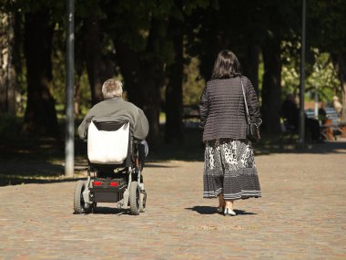 Bir kadın, elektrikli sandalyede seyahat eden bir adamla parkta yürüyor. İhtiyaç sahiplerinin velayeti. Kısıtlı hareket kabiliyetine sahip insanların faaliyetleri. Kas iskeleti sistemi hastalarının protezleri..