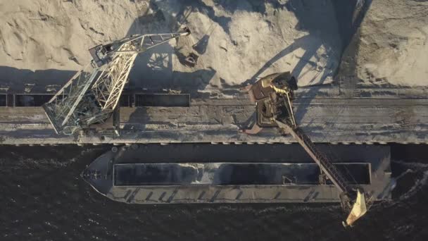 桟橋の近くの海岸に大規模なポートクレーン大規模なヒープに川の砂のバージをアンロードします バルク貨物の輸送のための列車 貨物港の仕事 空中写真ドローン四重曹 — ストック動画