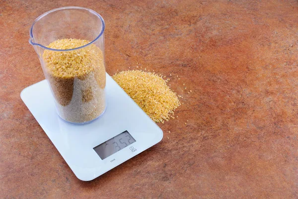 Зерно в мерной чашке на электронных весах с копировальным пространством — стоковое фото