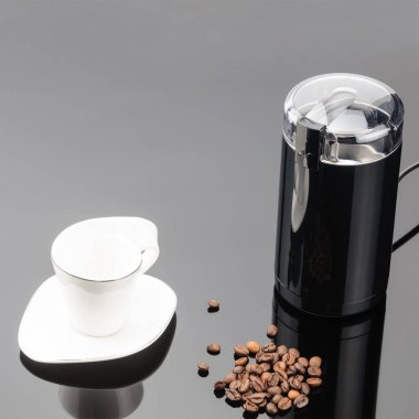 Gri ayna backg üzerinde coffe fasulye ve fincan ile Kahve öğütücü