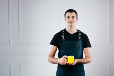 Garson, önlük giymiş kahve servisi yapıyor. Yeşil önlüklü garson. Müşteri için sarı kahve tutuyor.
