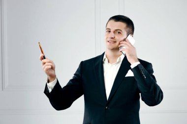 Elinde kalemle telefonla konuşan yakışıklı bir iş adamının portresi.