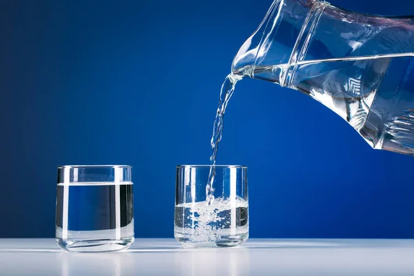 Hand pours water from jug into a glass isolated blue background