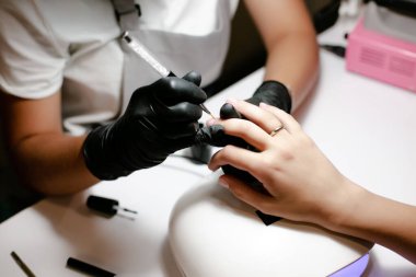 Kadın manikürcü güzellik salonunda manikür yaparken tırnaklarını törpülüyor ve şekillendiriyor.