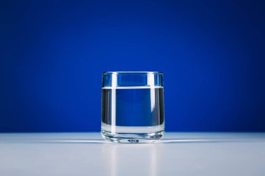 Mavi arkaplanda izole edilmiş bir bardak durgun su