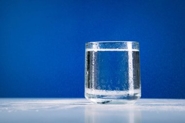 Mavi arkaplanda izole edilmiş bir bardak durgun su