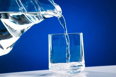 Mavi bir arka planda cam sürahide camdan cama su dökülüyor.