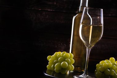 Tahta bir arka planda şarap şişesi, dolu bir bardak ve üzümler.