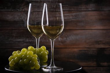 İki beyaz şarap kadehi ve ahşap arka planda bir masada üzüm.