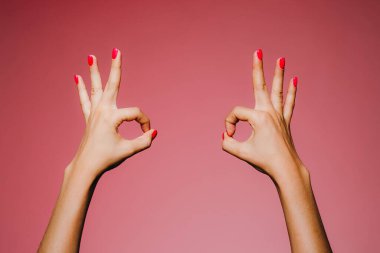 Pembe arka planda izole edilmiş parlak manikürlü bir kadının elleri.