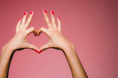 Parlak manikürlü bir kadının elleri pembe arka planda izole edilmiş aşk işareti parmakları