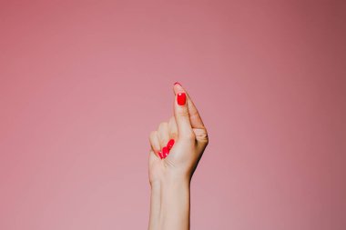 Pembe arka planda izole edilmiş parlak manikürlü bir kadın eli.