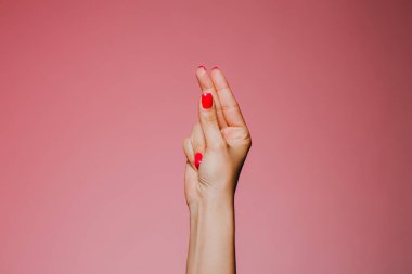 Pembe arka planda izole edilmiş parlak manikürlü bir kadın eli.