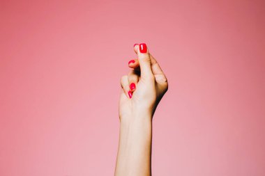 Pembe arka planda izole edilmiş parlak manikürlü bir kadın eli.