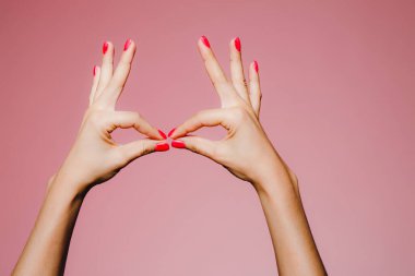 Pembe arka planda izole edilmiş, parlak manikürlü bir kadının elleri öpüşme hareketi.