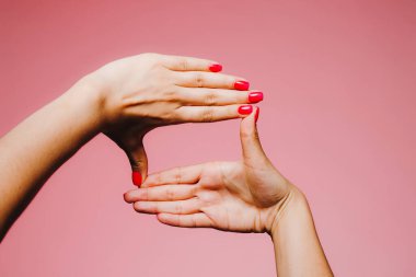 Pembe arka plan jestine izole edilmiş parlak manikürlü bir kadının elleri.