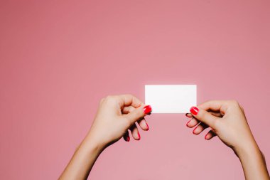 Kadının elleri pembe üzerine izole edilmiş boş bir kartvizit tutuyor.
