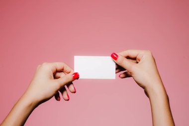 Kadının elleri pembe üzerine izole edilmiş boş bir kartvizit tutuyor.