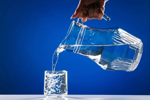 Hand Hälla Vatten Från Glas Kanna Till Glas Isolerad Blå — Stockfoto