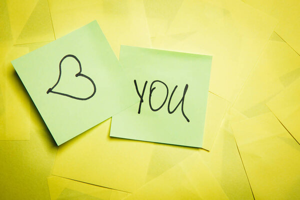 Two green sticky notes with word you and heart symbol on yellow notes