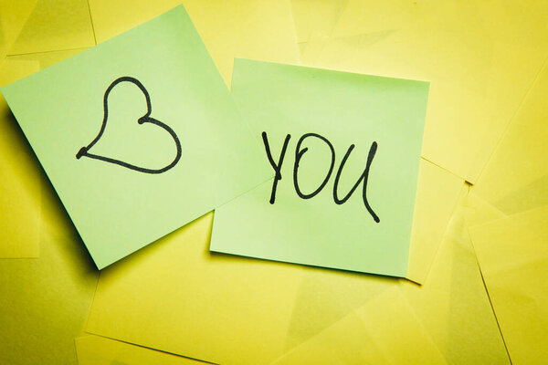 Two green sticky notes with word you and heart symbol on yellow notes
